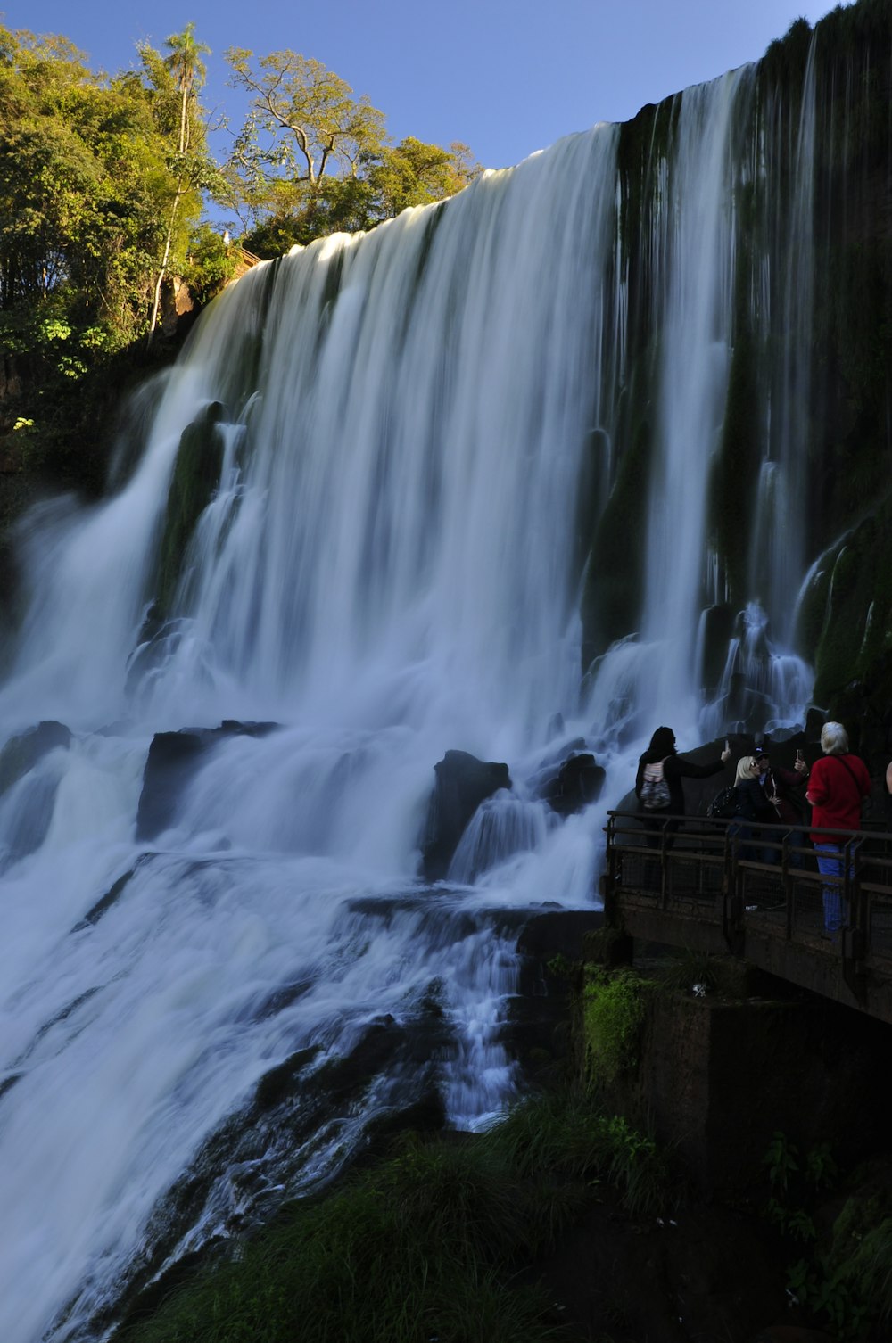 people sitting on brown wooden bench near waterfalls during daytime