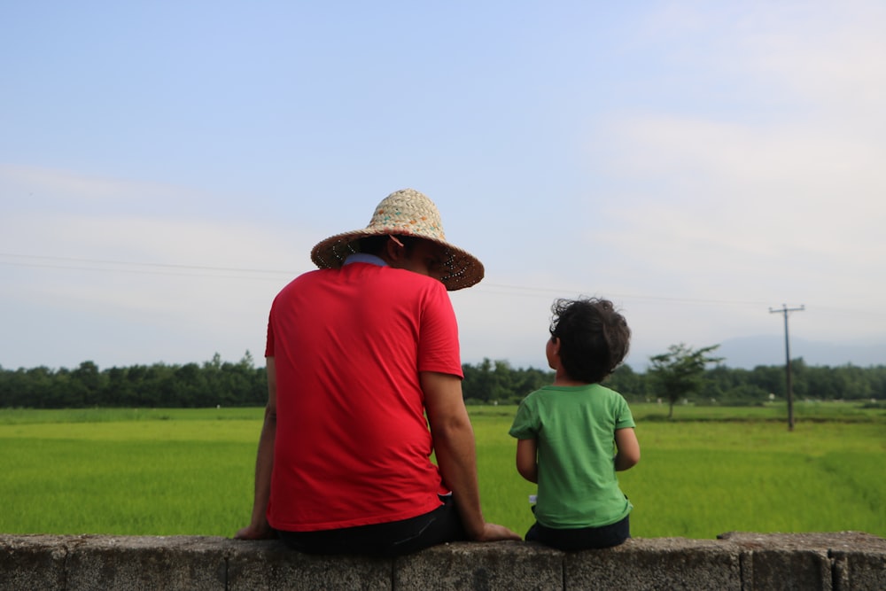 man in red polo shirt and brown straw hat sitting beside woman in green t-shirt