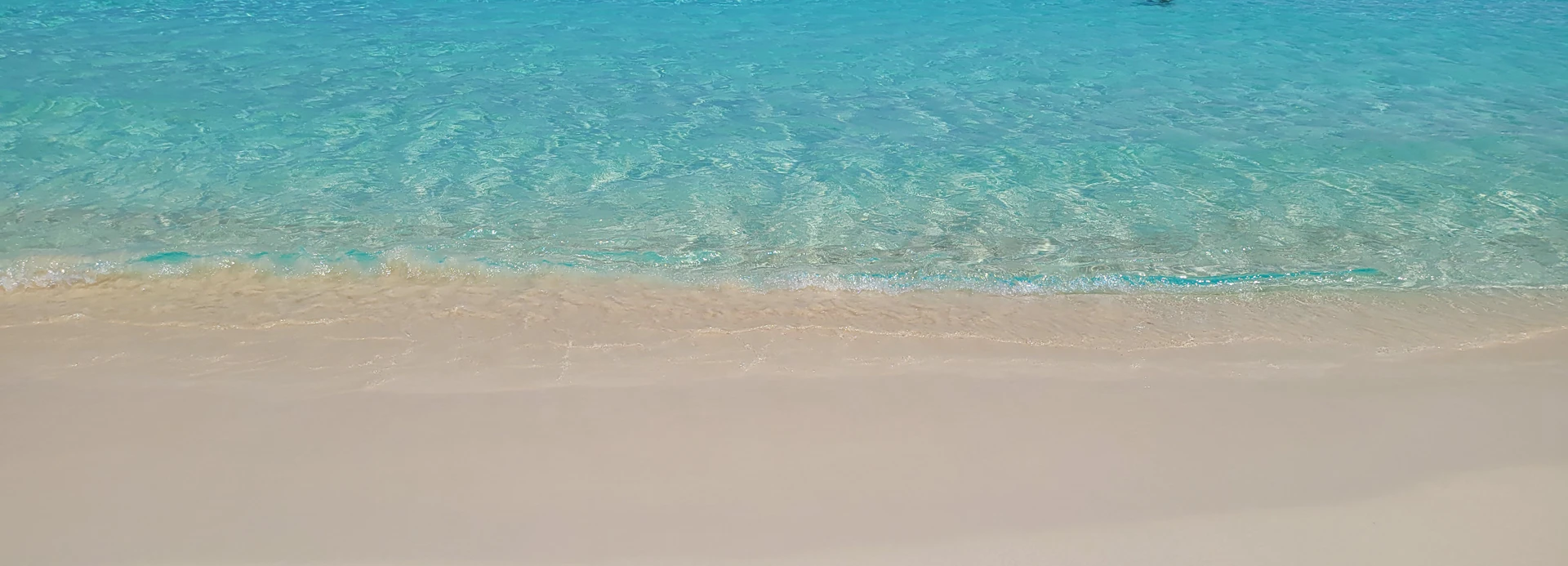 A crystal-clear turquoise beach with gentle waves lapping against white sand, inviting peaceful relaxation.