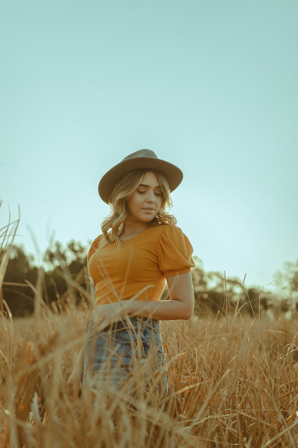 woman in yellow polo shirt and blue denim jeans wearing brown hat standing on brown grass