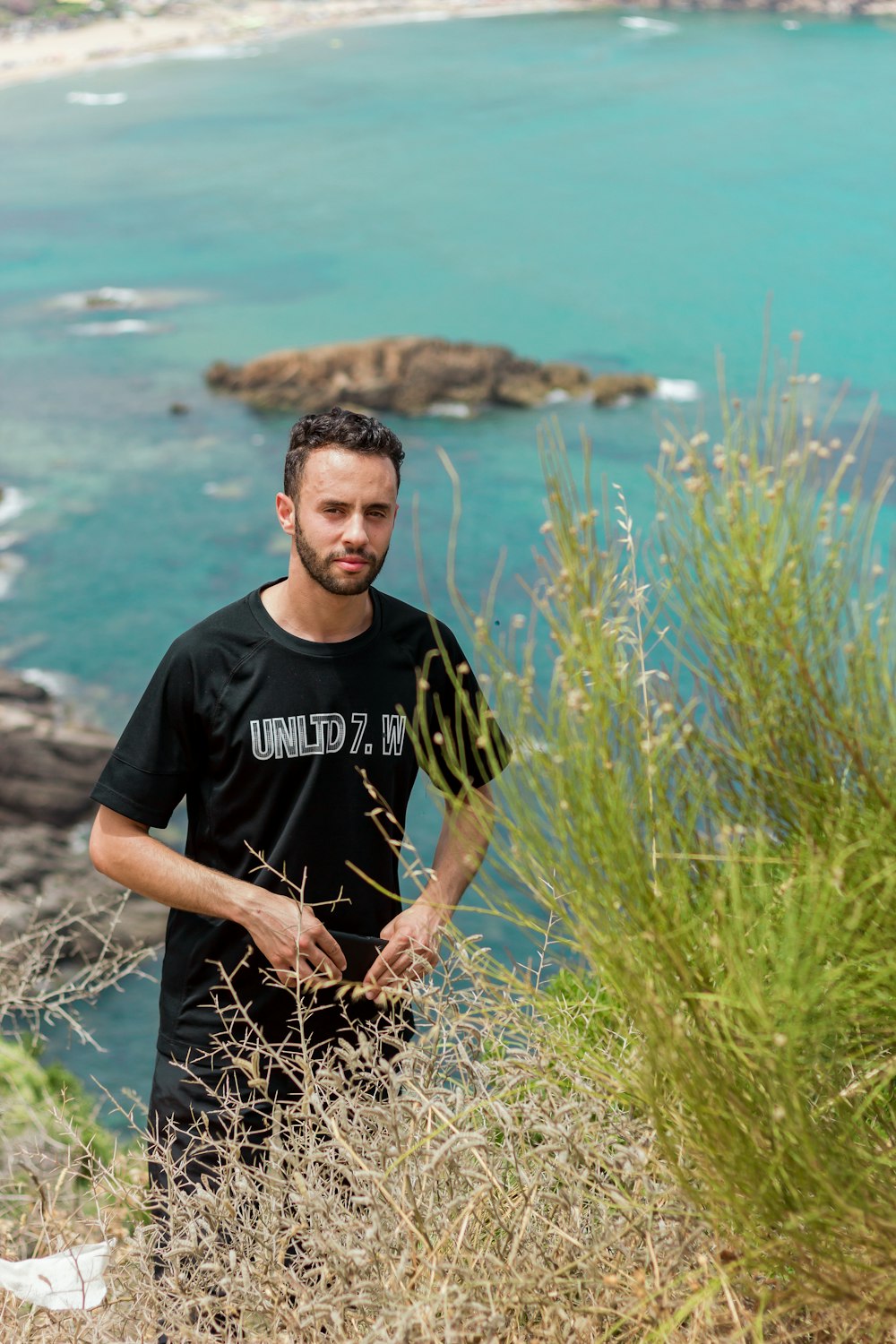 man in black crew neck t-shirt standing on green grass field near body of water