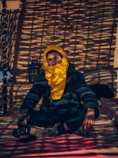 man in black jacket and yellow knit cap sitting on brown wooden bench
