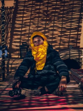 man in black jacket and yellow knit cap sitting on brown wooden bench