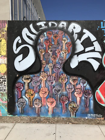 Colorful mural depicting hands joined in solidarity against a bright blue sky.