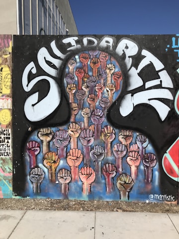 A mural depicting numerous raised fists in various skin tones, symbolizing unity and strength. The word 'Solidarity' is painted in large, stylized letters above the fists, conveying a message of togetherness and support.