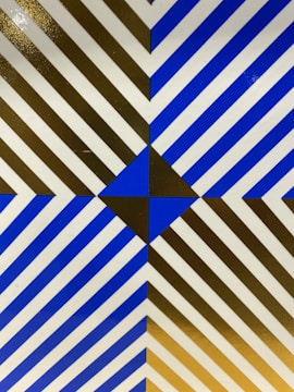An optical art design with diagonal stripes creating a geometric pattern. The central focus is a blue diamond shape at the intersection of the stripes, which are alternately blue and brown with white spacings.