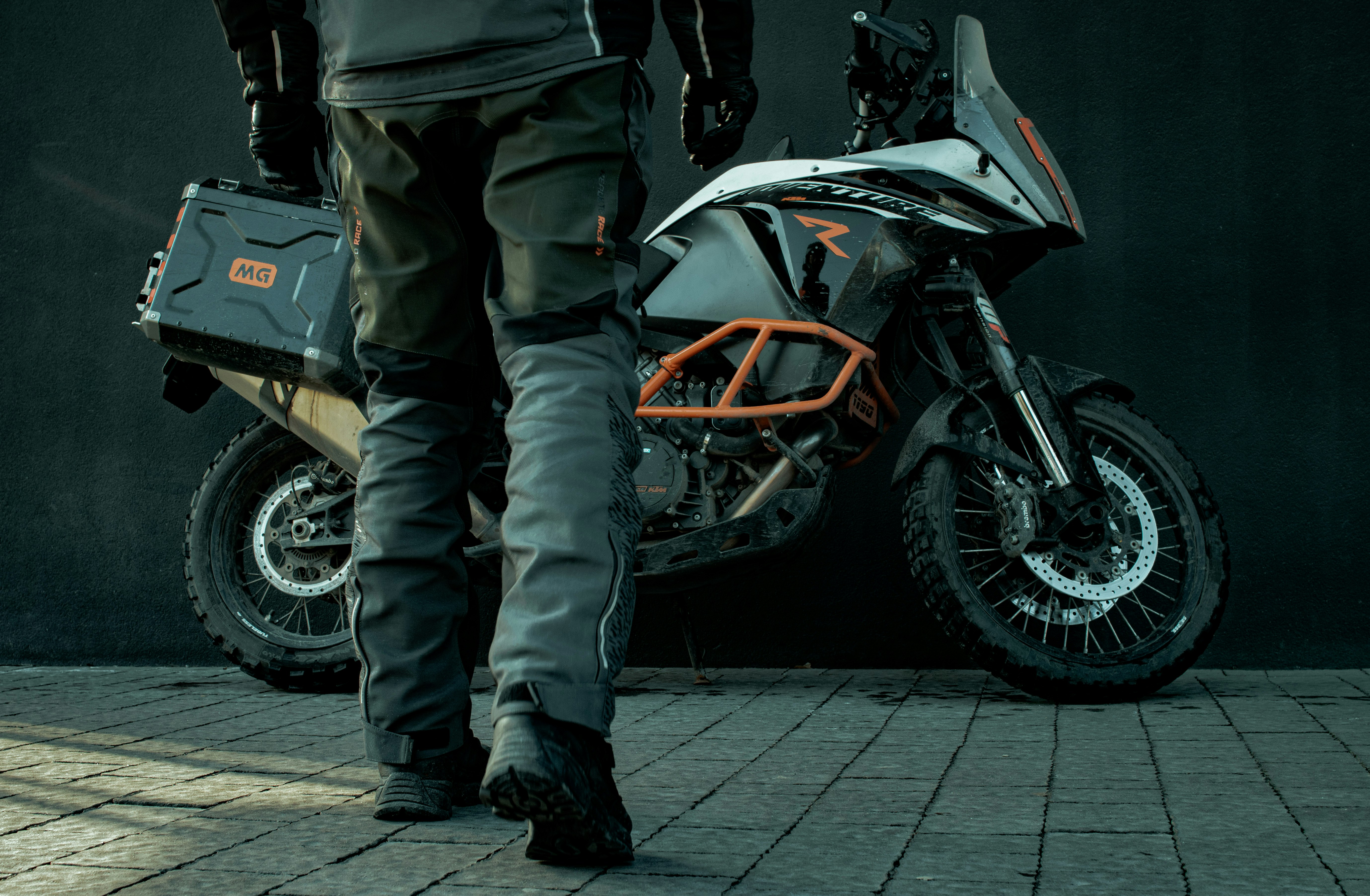 man in black leather jacket and gray pants standing beside black and orange sports bike during
