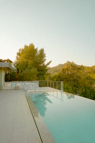A sleek, modern infinity pool overlooking a serene sunset-lit backyard.
