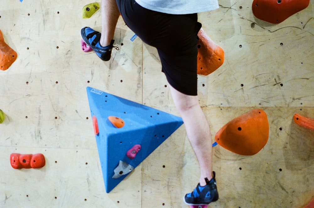 person in black shorts and blue and black flip flops standing on blue and orange plastic