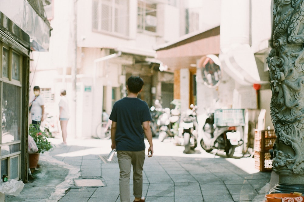 man in black t-shirt walking on sidewalk during daytime