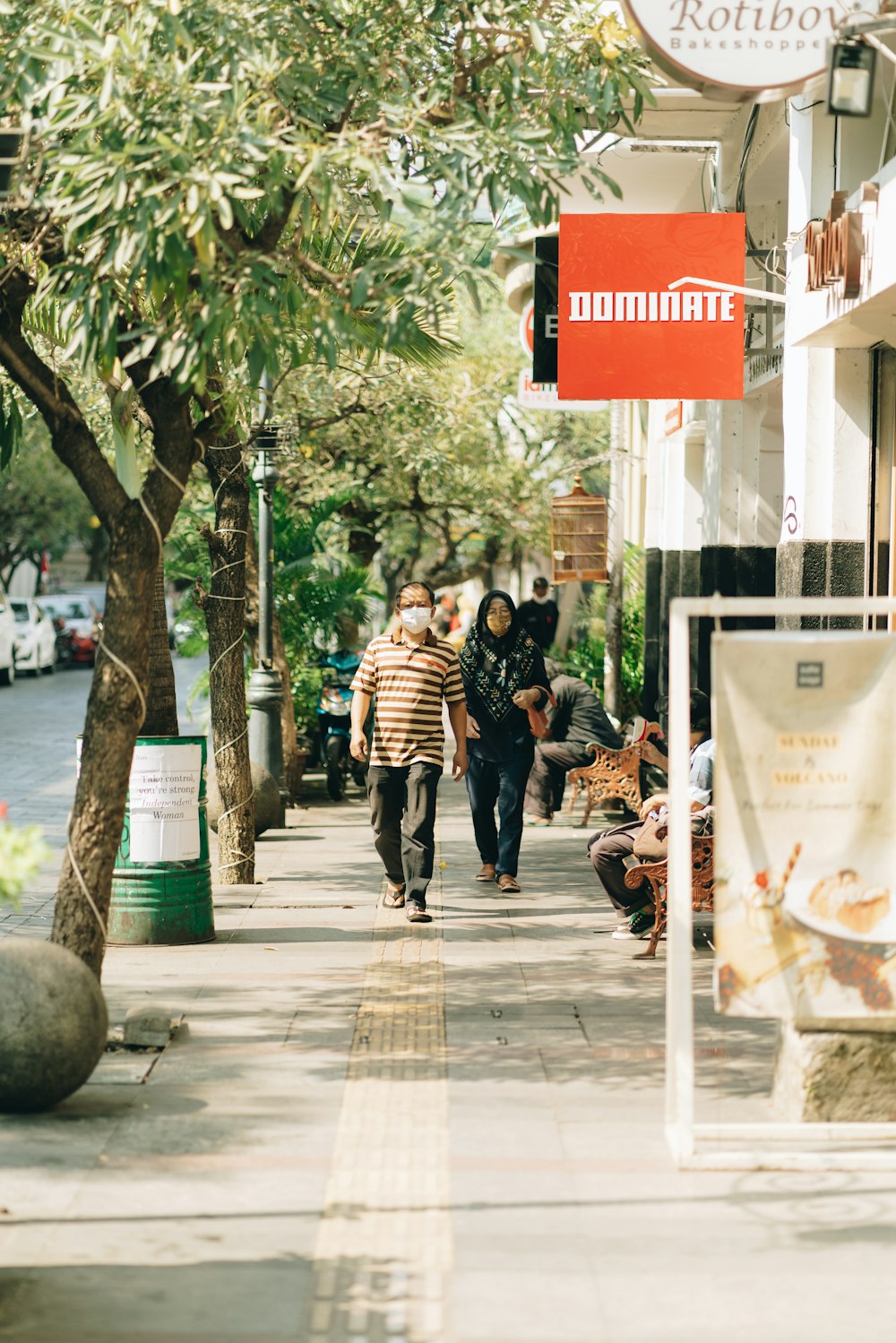 people walking on sidewalk near trees and building during daytime