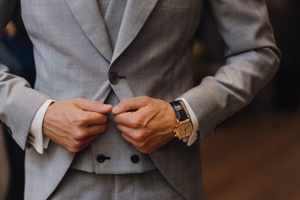 homme en veste de costume grise portant une montre analogique or et blanc