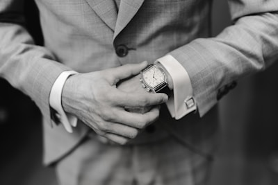 A stylish man adjusting his cufflinks while wearing a classic suit and watch.