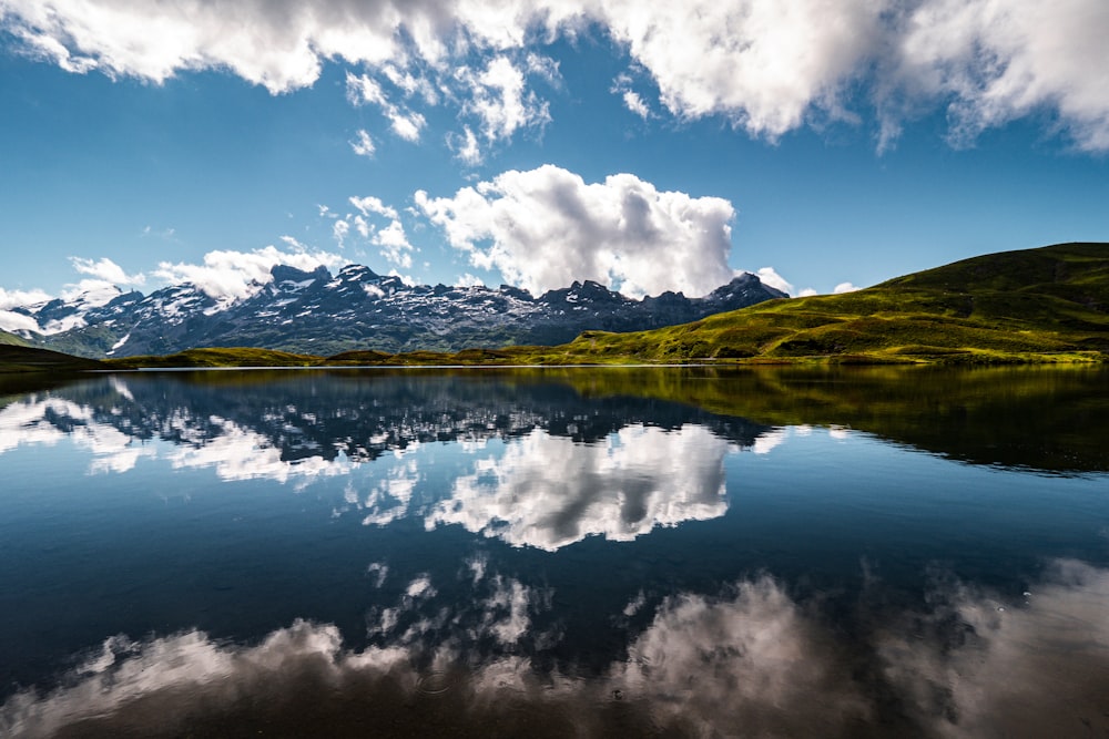 Montagna verde accanto allo specchio d'acqua sotto il cielo blu e le nuvole bianche durante il giorno