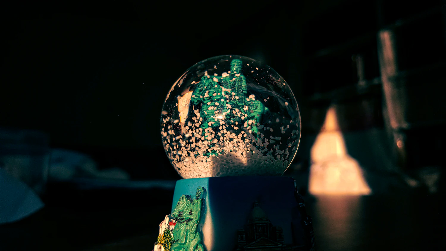 A snow globe glittering green in the dark beside a lit candle