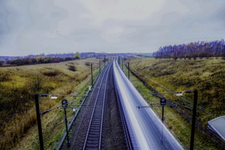gray train rail near green grass field during daytime