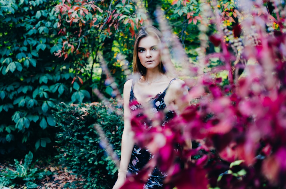 woman in pink tank top standing beside red flowers