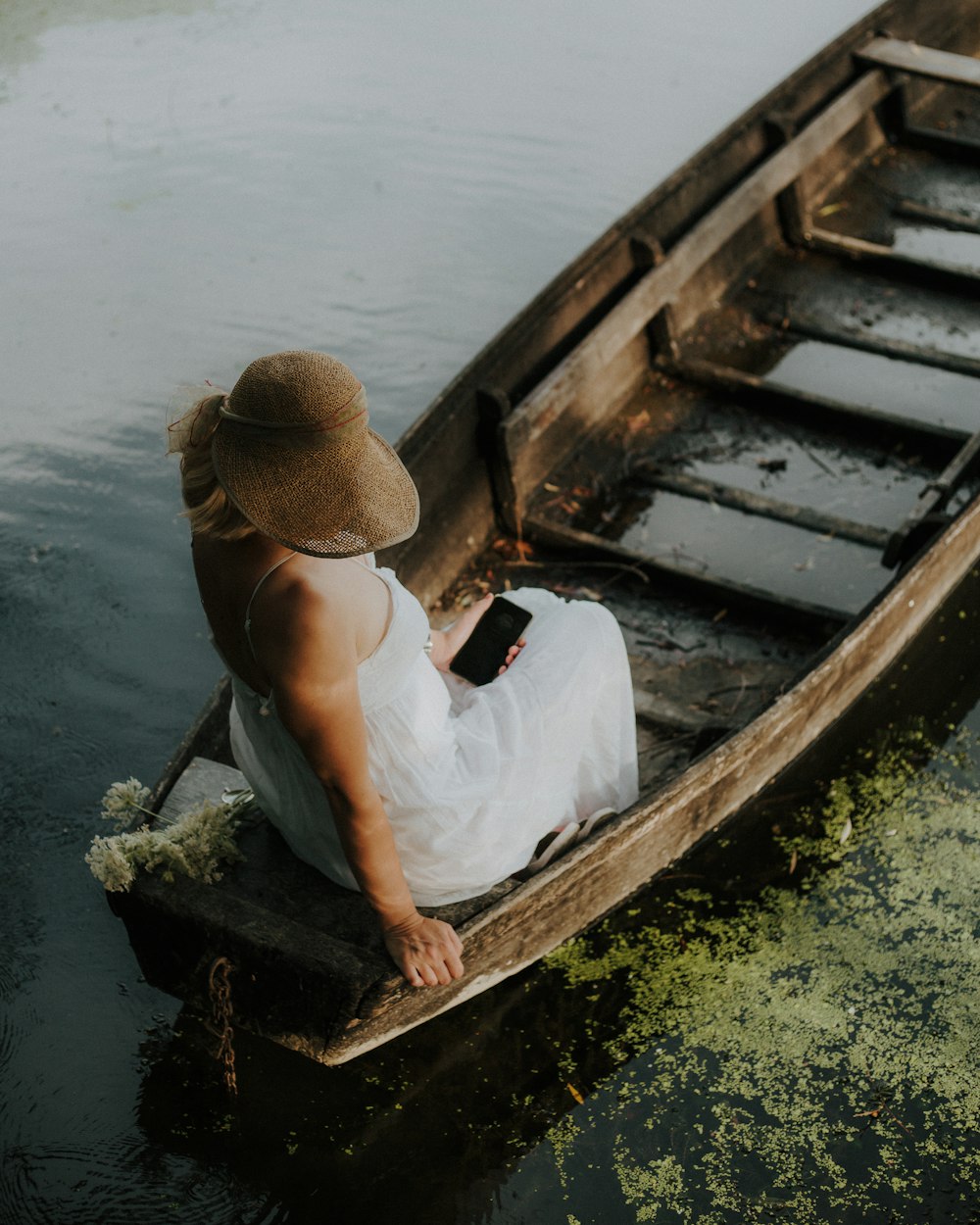 man in white tank top sitting on brown wooden boat during daytime