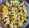A bowl filled with a mixture of puffed rice, lentils, spices, and assorted savory items is displayed, showcasing a colorful and textured assortment of a traditional Indian snack.