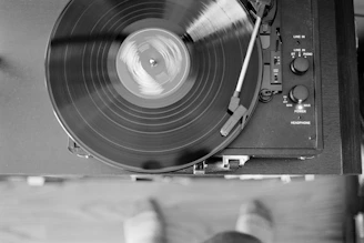 Black and white photo of a vinyl record spinning on a turntable in a minimalist studio setting.