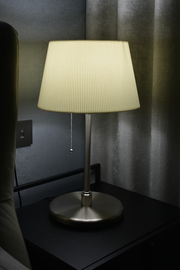 A bedside table softly lit by a sleek, decorative table lamp.