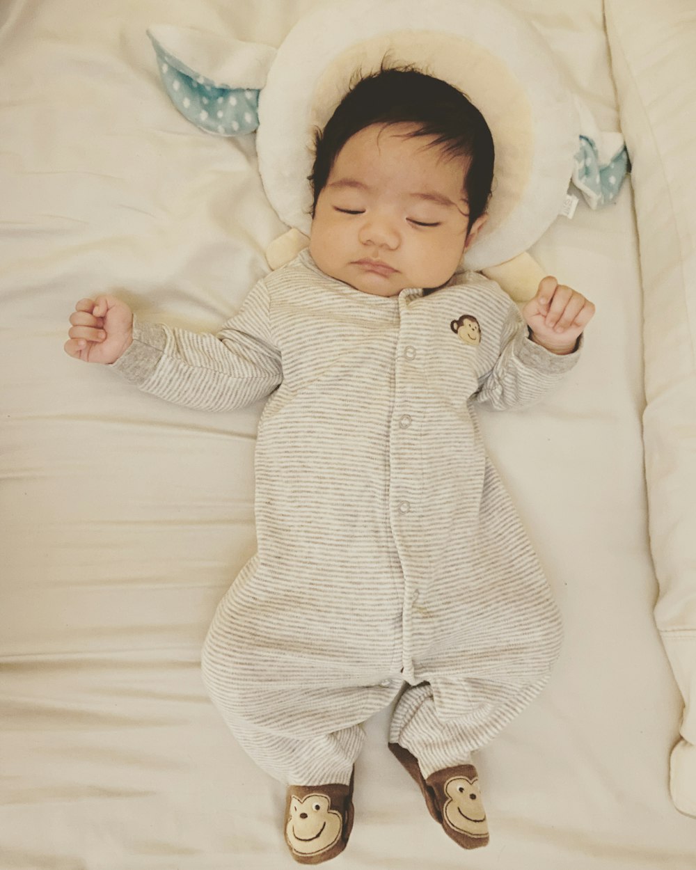 baby in white and green onesie lying on white textile