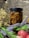 A jar filled with honeycomb sits in natural lighting against a rustic stone background. Surrounding the jar are sprigs of dried flowers and fresh lavender, alongside a couple of red apples.