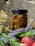 A jar filled with honeycomb sits in natural lighting against a rustic stone background. Surrounding the jar are sprigs of dried flowers and fresh lavender, alongside a couple of red apples.