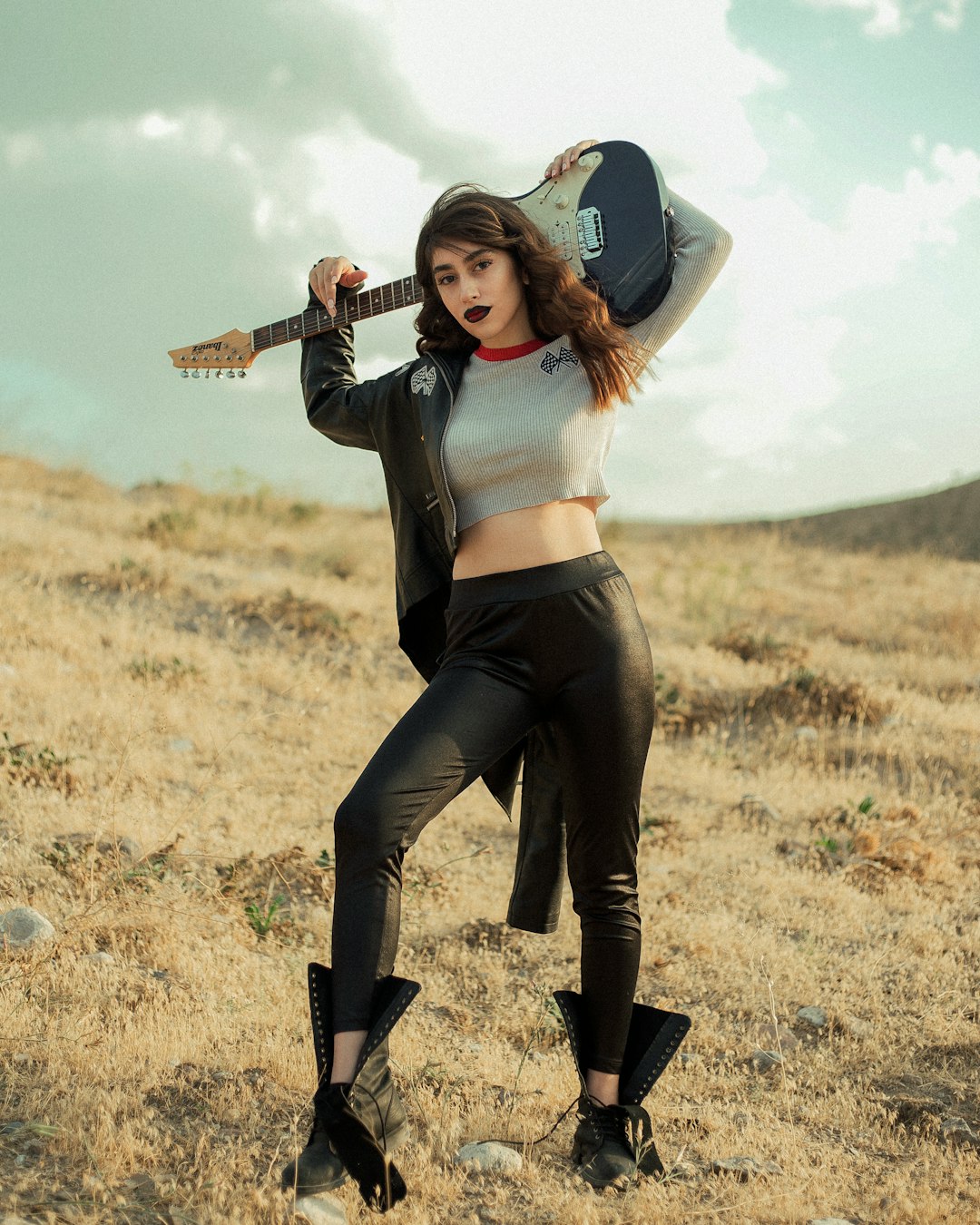 woman in white long sleeve shirt and black pants holding brown acoustic guitar