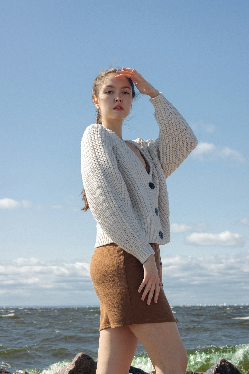 mulher no suéter de malha branco e shorts marrons de pé sob o céu azul durante o dia