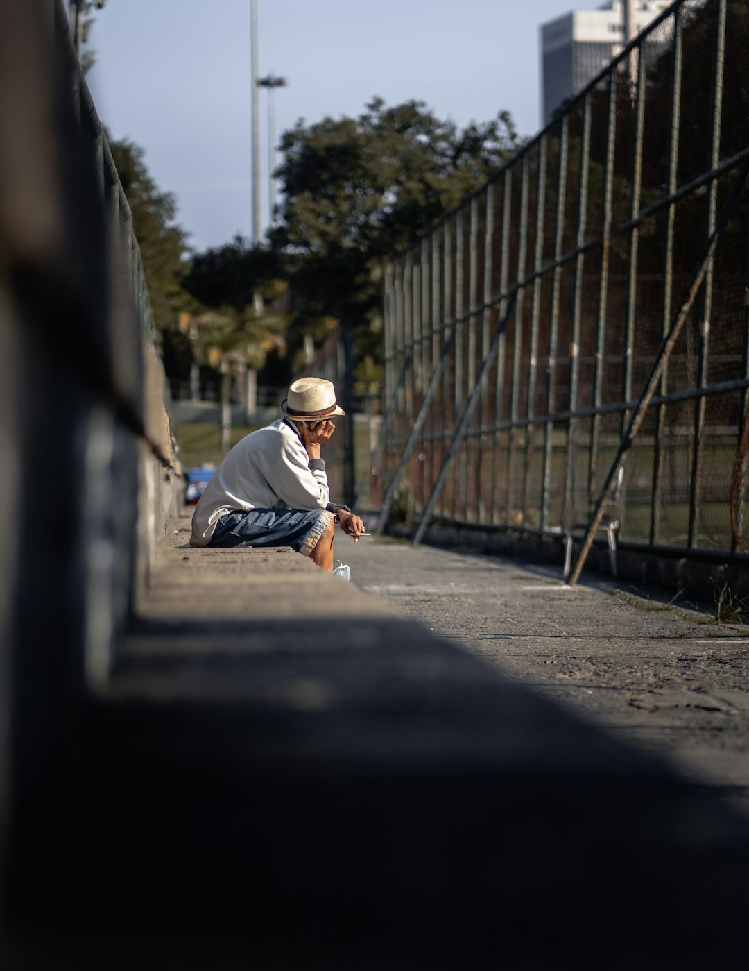 man in white t-shirt and blue denim jeans sitting on concrete road during daytime