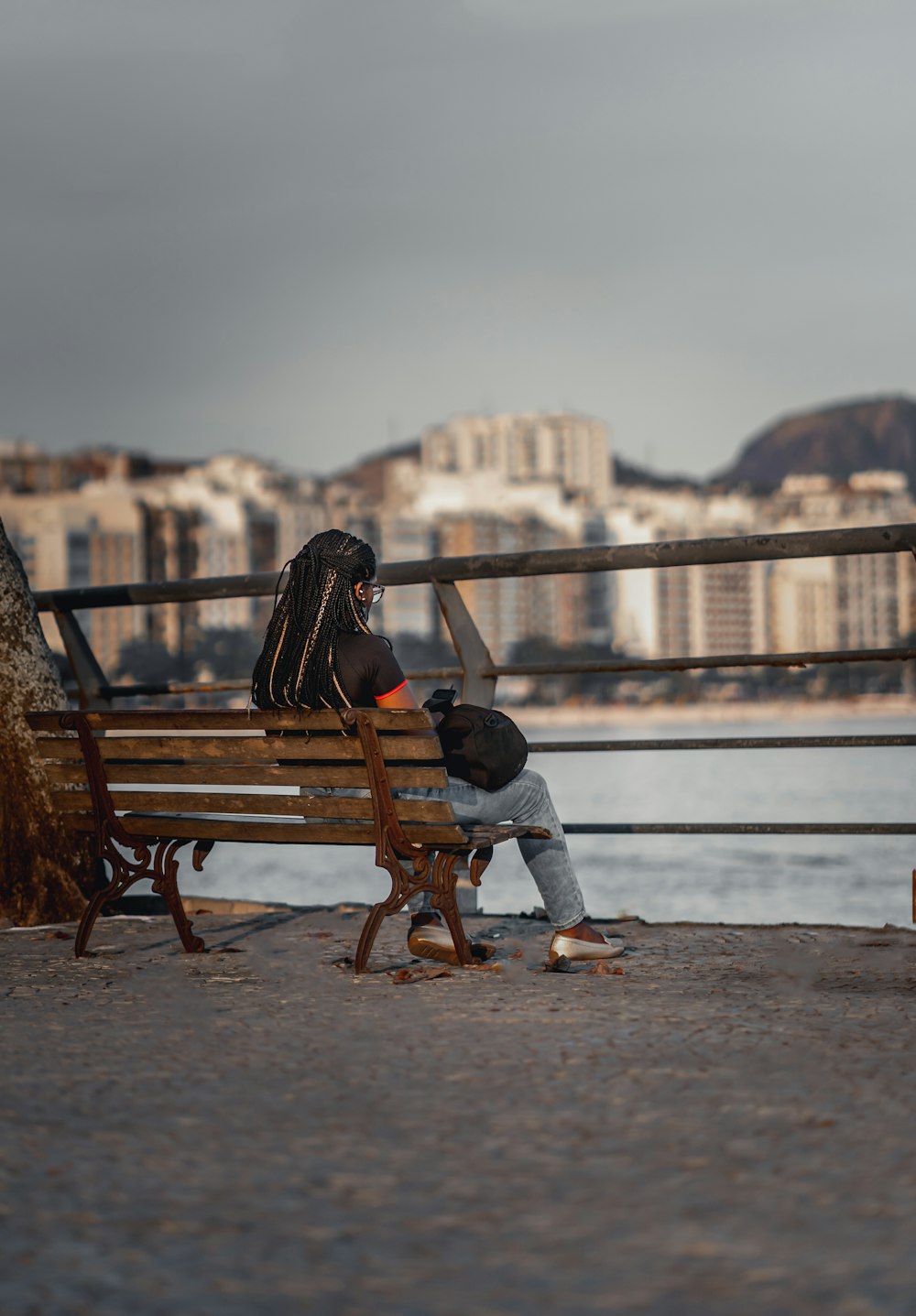 昼間、茶色の木製のベンチに座る黒いジャケットを着た女性