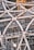 Detailed view of a complex steel structure with interconnected metal beams and support scaffolding. Numerous pipes and girders crisscross in a geometric pattern, accompanied by visible construction elements such as scaffolding and a yellow crane in the background. The scene captures an intricate industrial design, showcasing the framework of a developing building or structure.