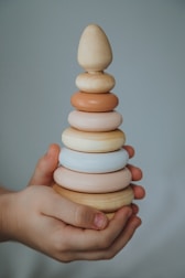 A pair of hands holding a wooden stacking toy composed of seven rings in varying sizes and colors, arranged from largest at the bottom to smallest on top.