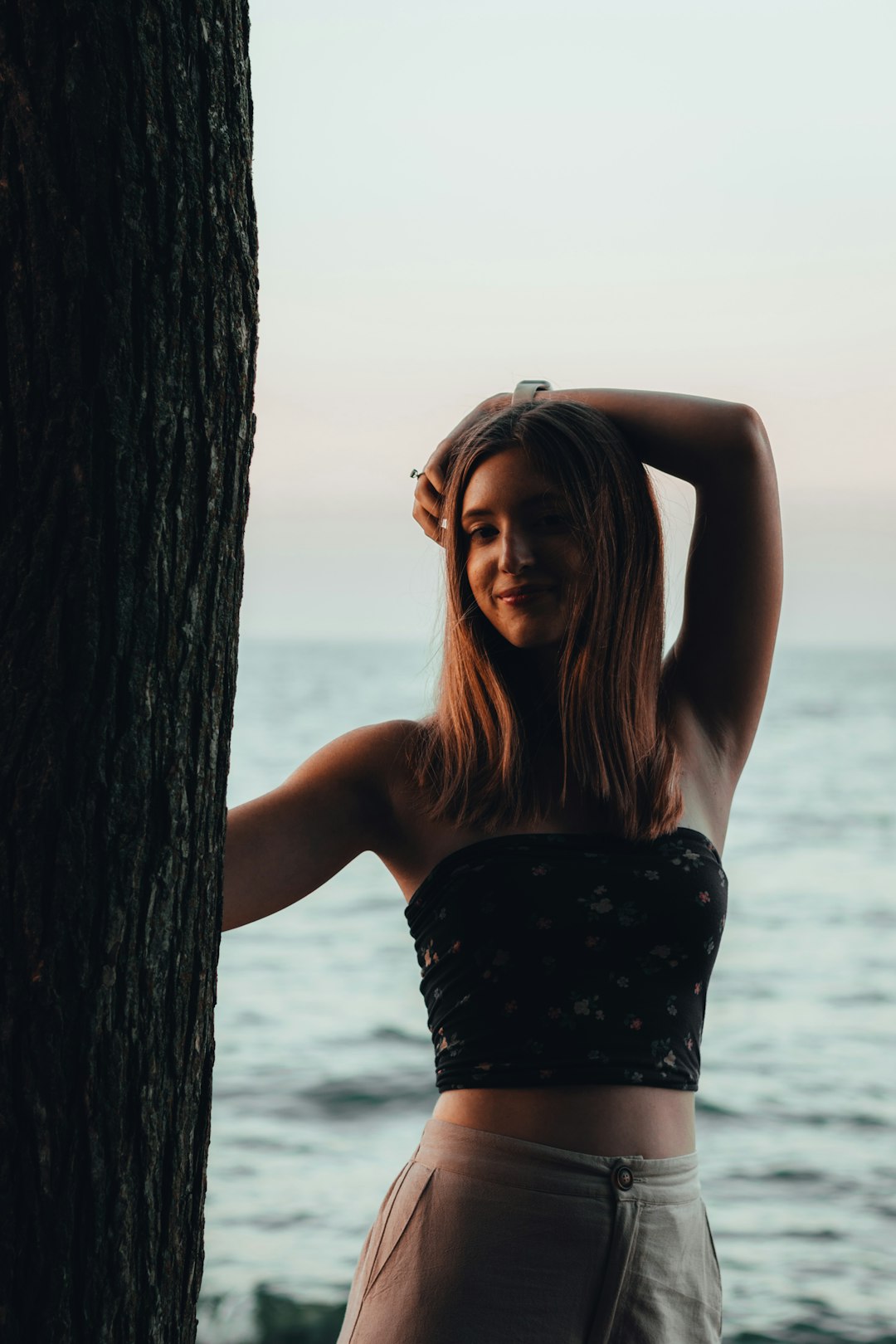 woman in black tube top leaning on brown tree trunk during daytime