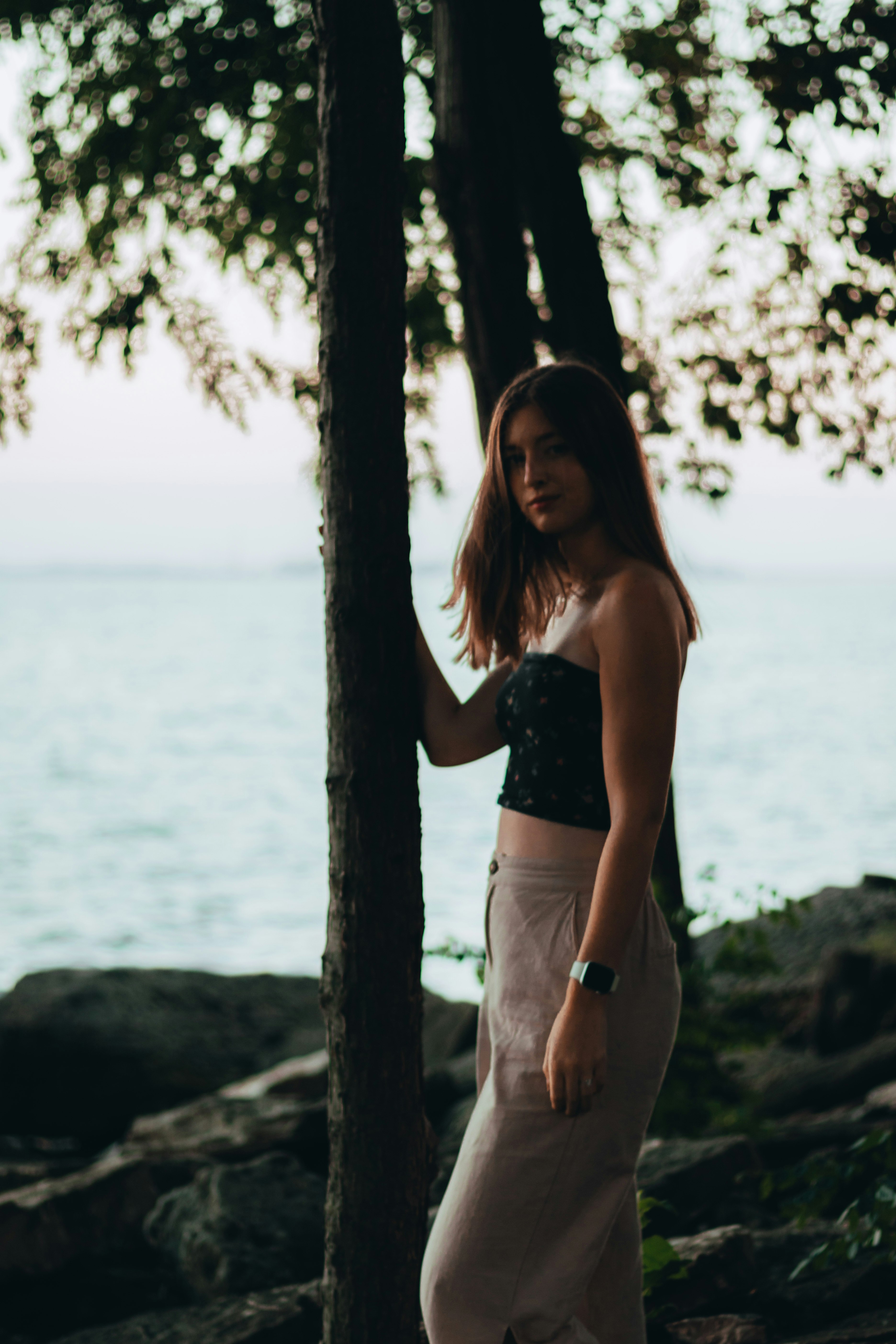 woman in black tank top and white shorts standing beside tree during daytime