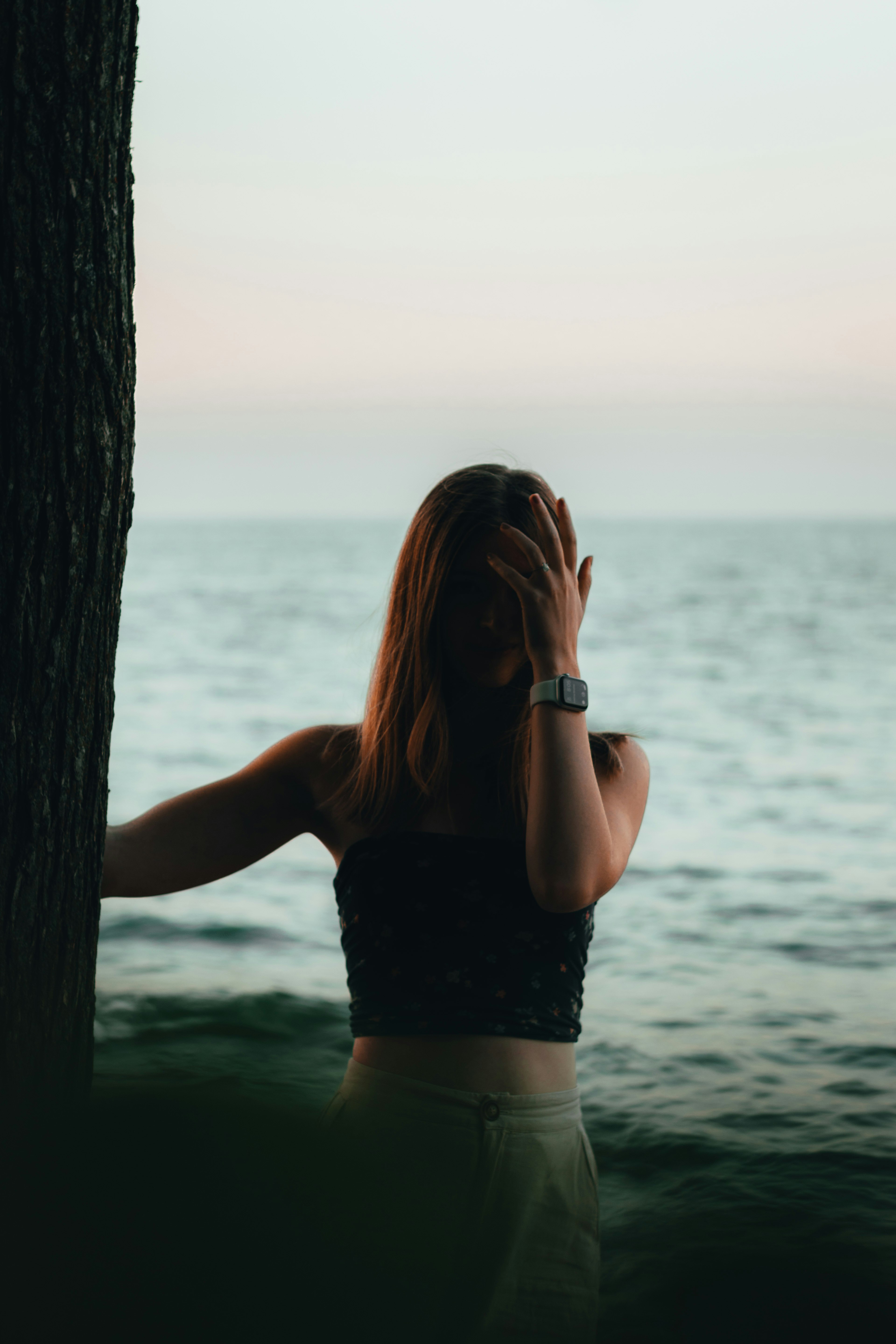 woman in black crop top and blue denim daisy dukes standing beside tree trunk during daytime