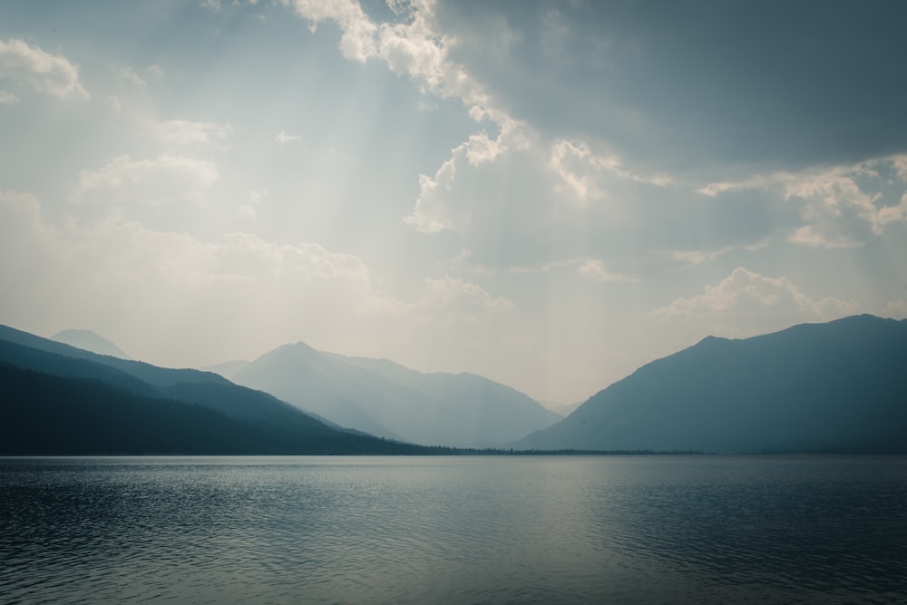 body of water near mountain under white clouds and blue sky during daytime