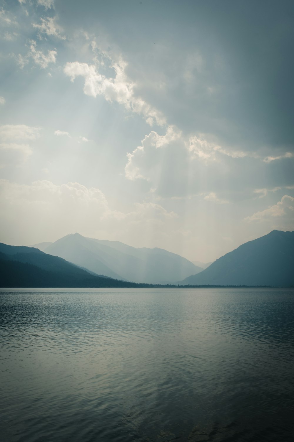 body of water near mountain under white clouds during daytime