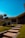 A modern house with a sloped roof and large windows, surrounded by a neatly landscaped garden featuring trimmed bushes and a small tree. The pathway to the entrance consists of evenly spaced stone steps bordered by grass, under a clear blue sky that enhances the serene ambiance.