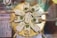 Nine decorative ice cream bars arranged in a circular pattern on a golden platter. Each ice cream bar is coated in a pale green or white glaze and adorned with gold foil and decorative pieces such as edible flowers and green beads.