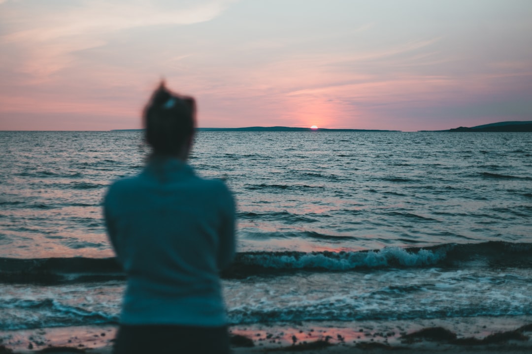 woman in green shirt standing on seashore during sunset