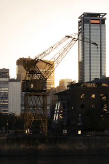 A powerful 25-ton hydraulic crane lifting heavy steel beams at a bustling Mumbai construction site during sunset.