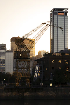 A powerful 100-ton crane lifting steel beams against a city skyline at dusk.