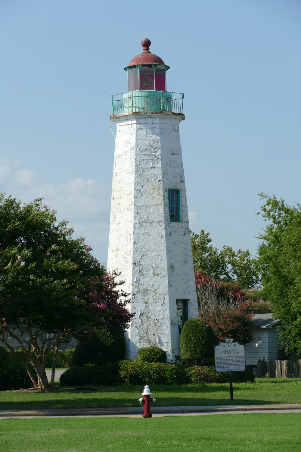 white and red lighthouse near green trees under blue sky during daytime