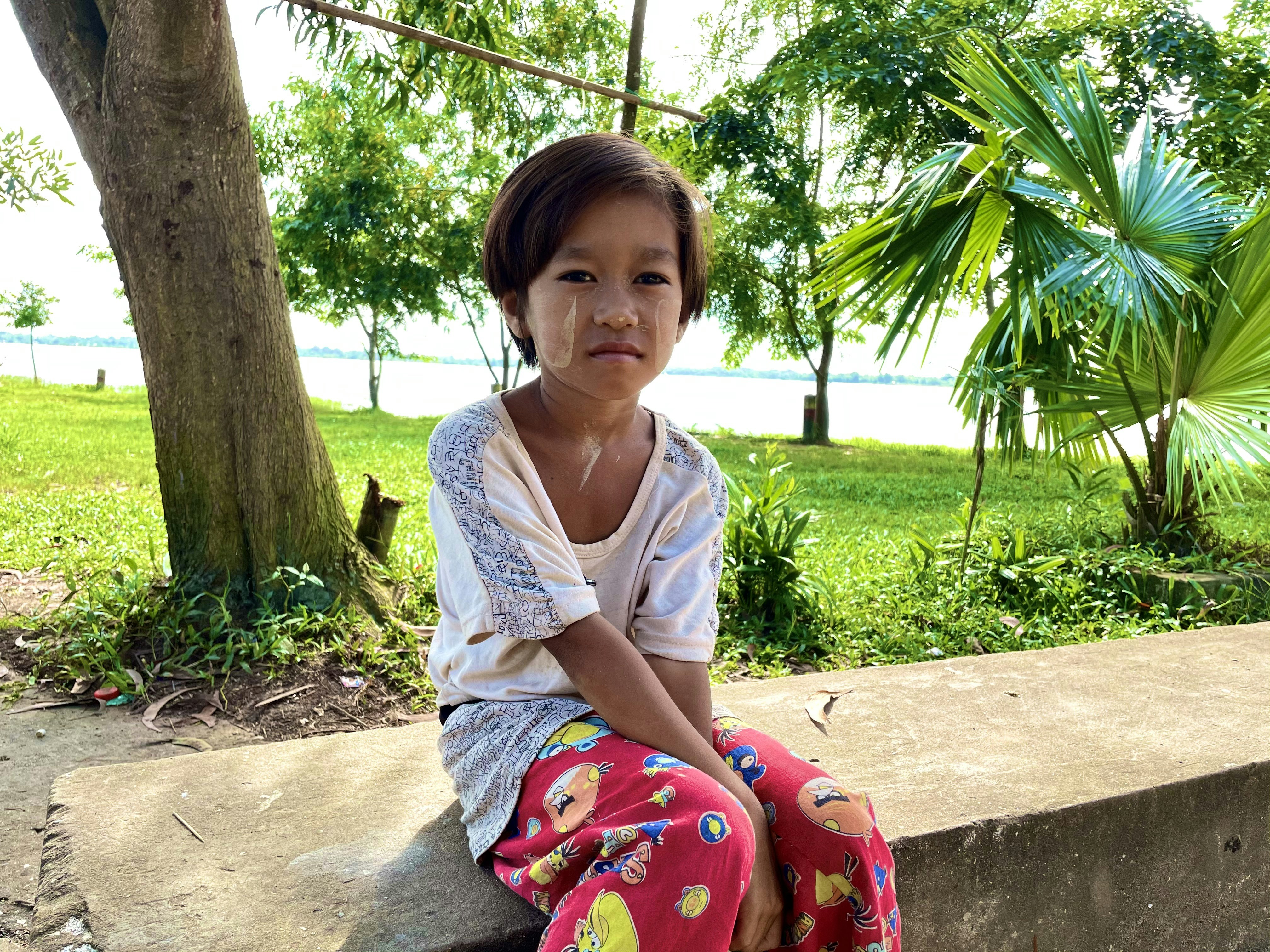Muchacha en vestido floral blanco y rosa sentada en piso de concreto gris