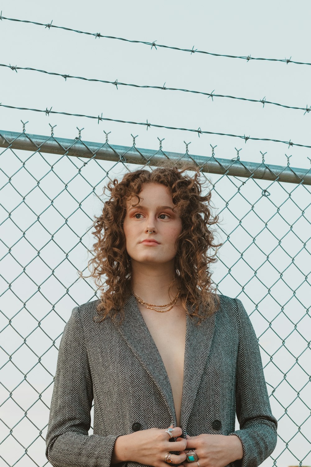 woman in gray coat standing beside gray metal fence during daytime