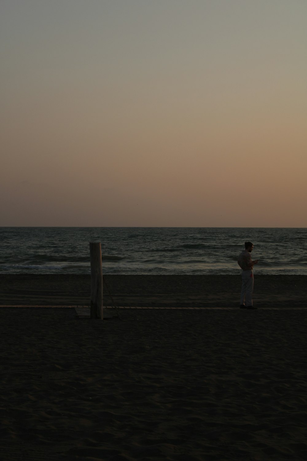 Mujer en vestido blanco de pie en la playa durante la puesta del sol