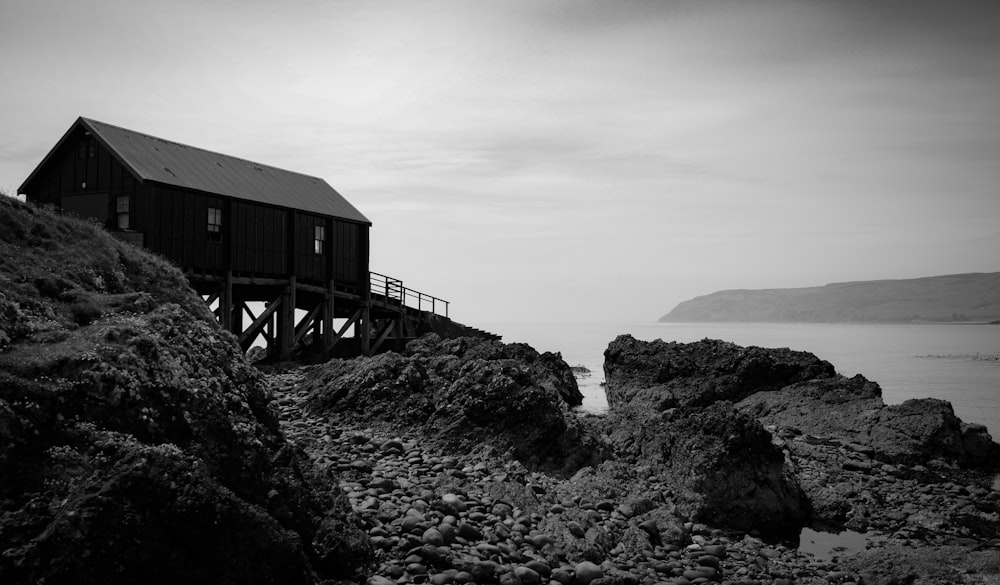 grayscale photo of wooden house on rocky hill
