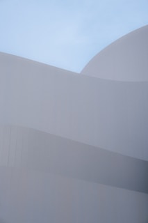 Smooth, curved architectural forms composed of subtle, overlapping layers create a sense of harmony against a clear blue sky. The minimalist design emphasizes clean lines and geometric precision, with a focus on texture and light.